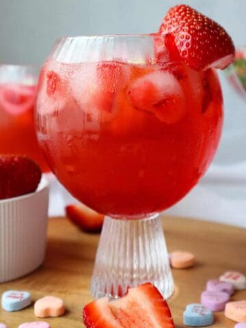 A glass of Strawberry Vanilla Margarita with candy and strawberries around it.
