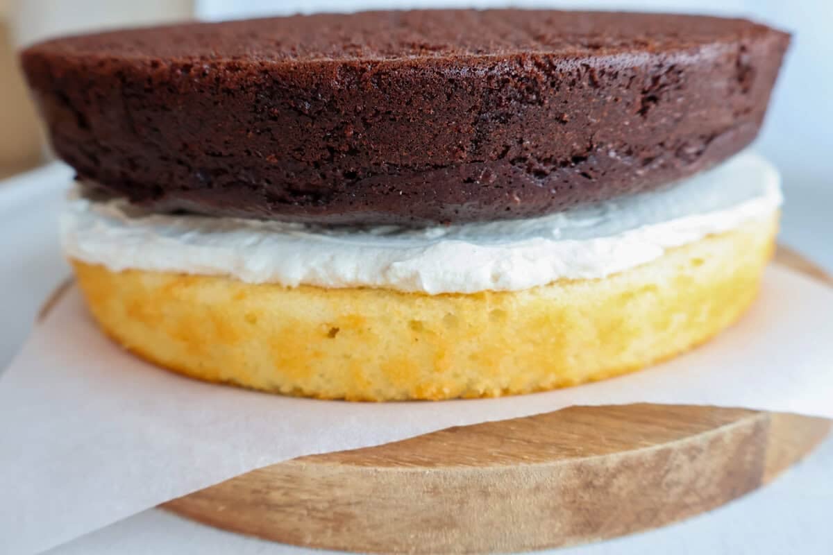 A chocolate and vanilla cake being layered and frosted.