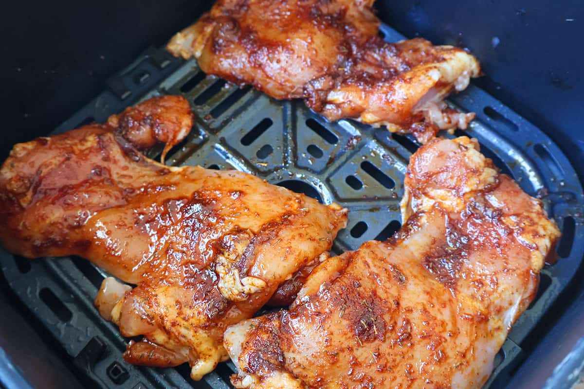 Three seasoned boneless chicken thighs in an air fryer basket.