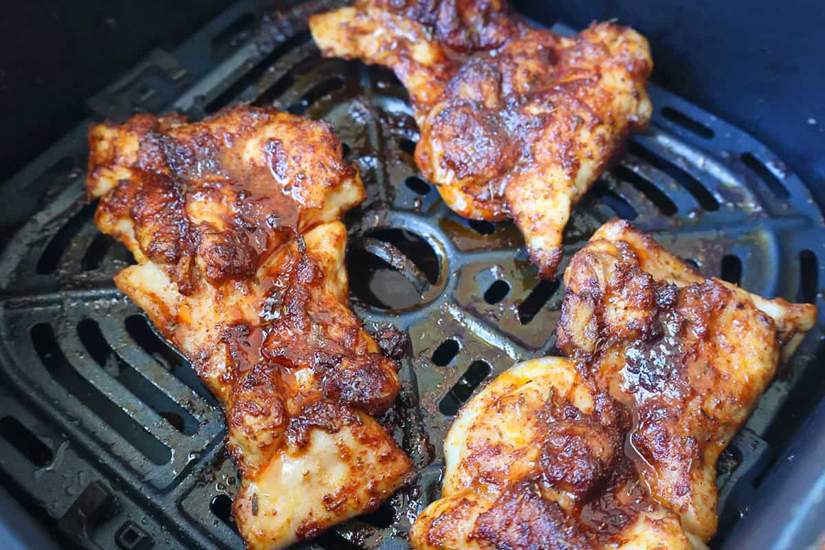 Four cooked boneless chicken thighs in an air fryer basket.