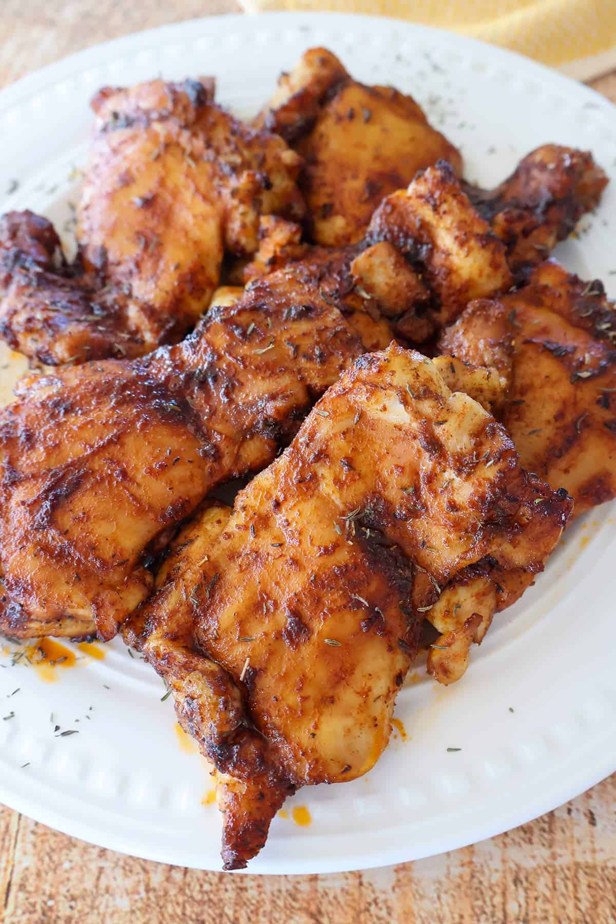 A white plate with a piel of cooked chicken thighs.