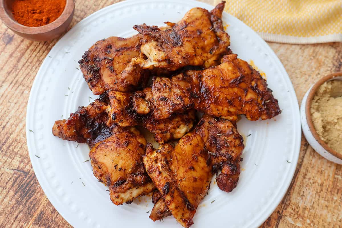 A white plate filled with cooked chicken thighs.