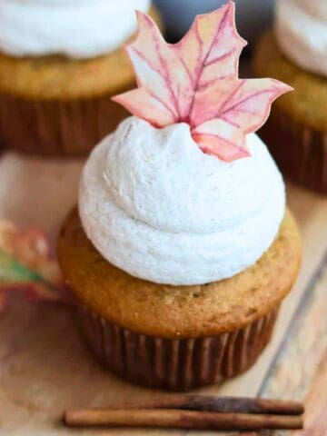 Frosted banana cupcakes on cutting board with cinnamon sticks.