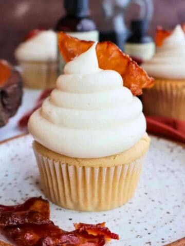 A maple bacon cupcake surrounded by bacon and other cup cakes.