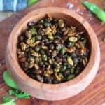 A brown bowl full of crispy edamame with green garnish.