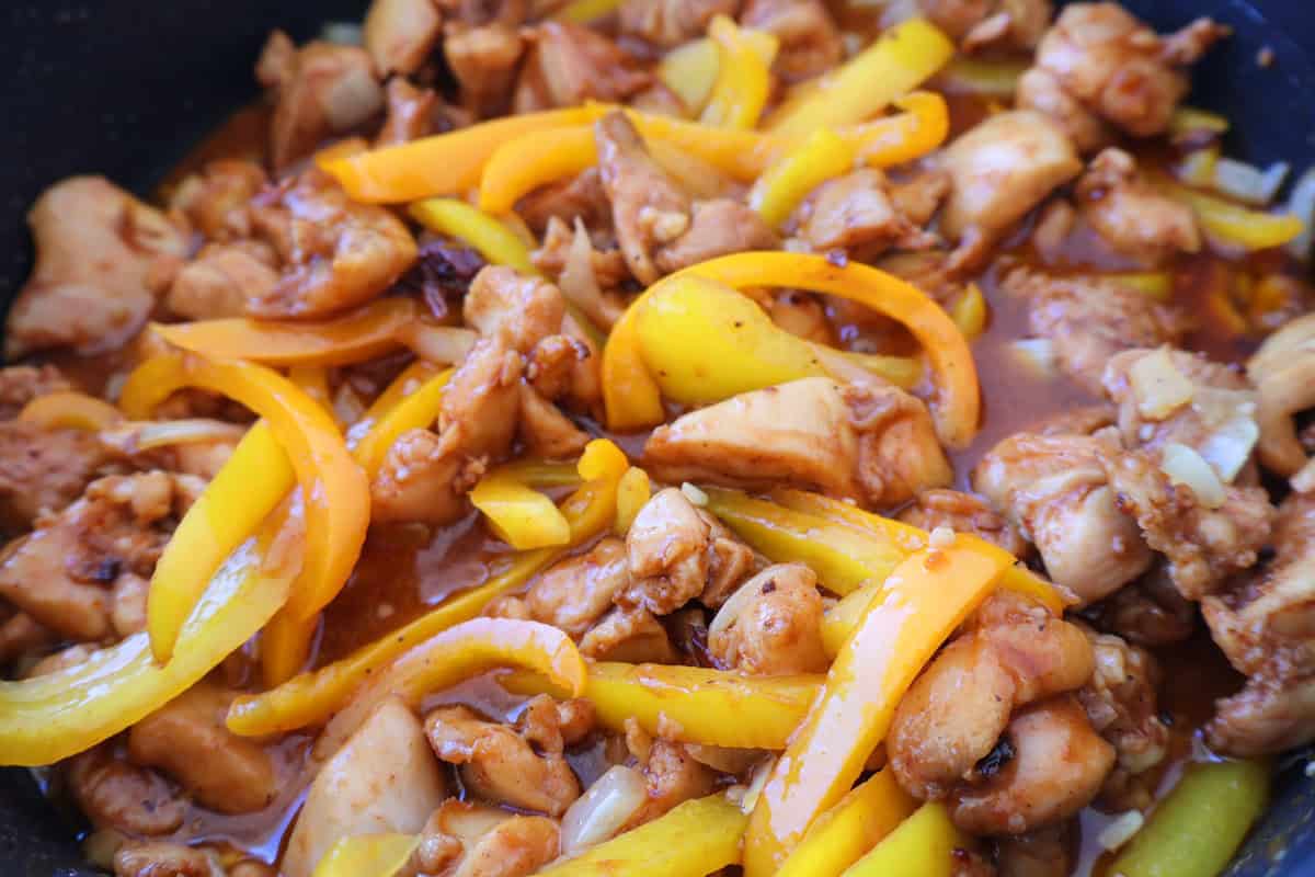 Skillet full of chicken and bell pepper slices.
