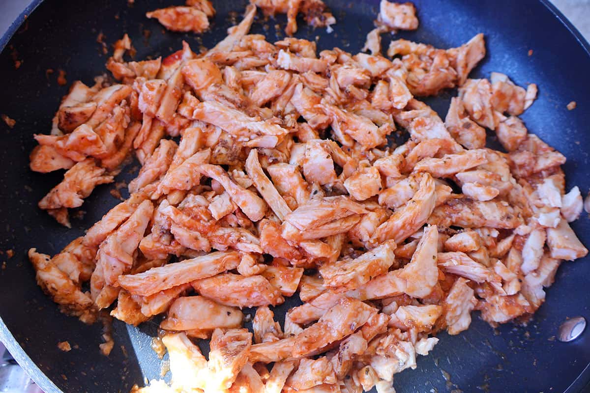 A pan full of cooked diced chicken with salsa. 
