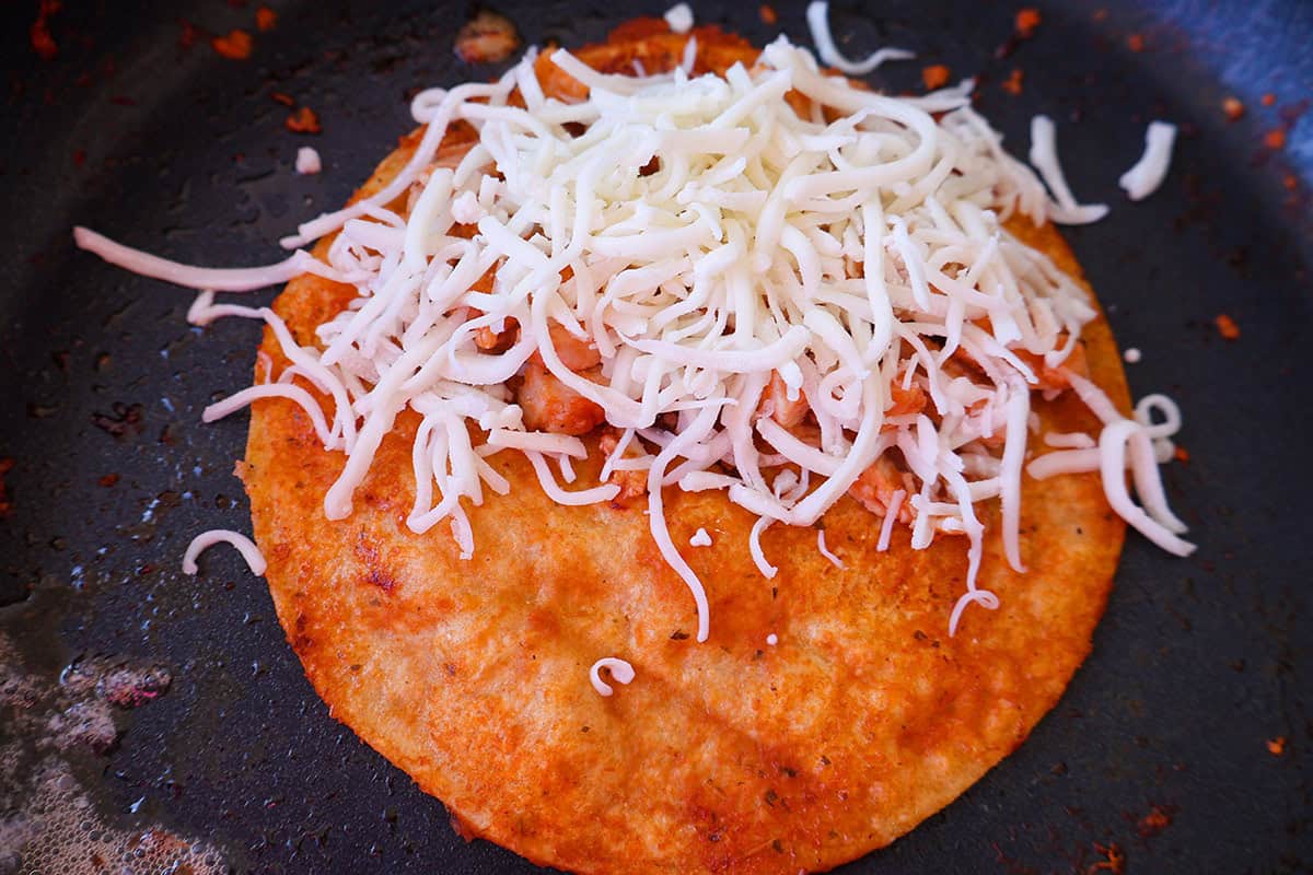 A corn tortilla topped with chicken and cheese in a pan. 