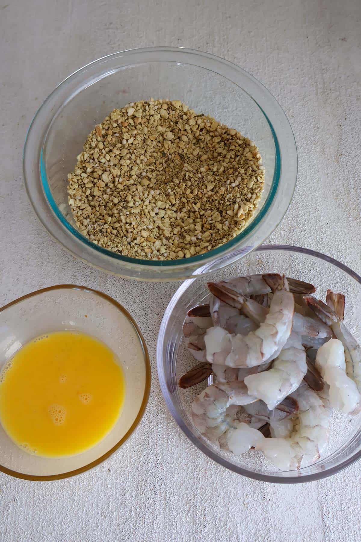 An overhead shot of bowls of shrimp, panko, and egg. 