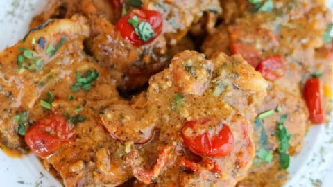 A serving dish with four chicken thighs in tomato sauce.