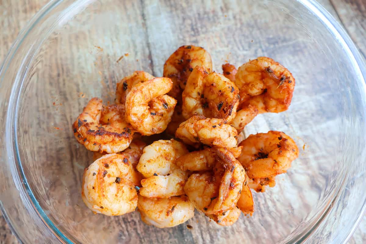 A glass bowl with seasoned cooked shrimp.