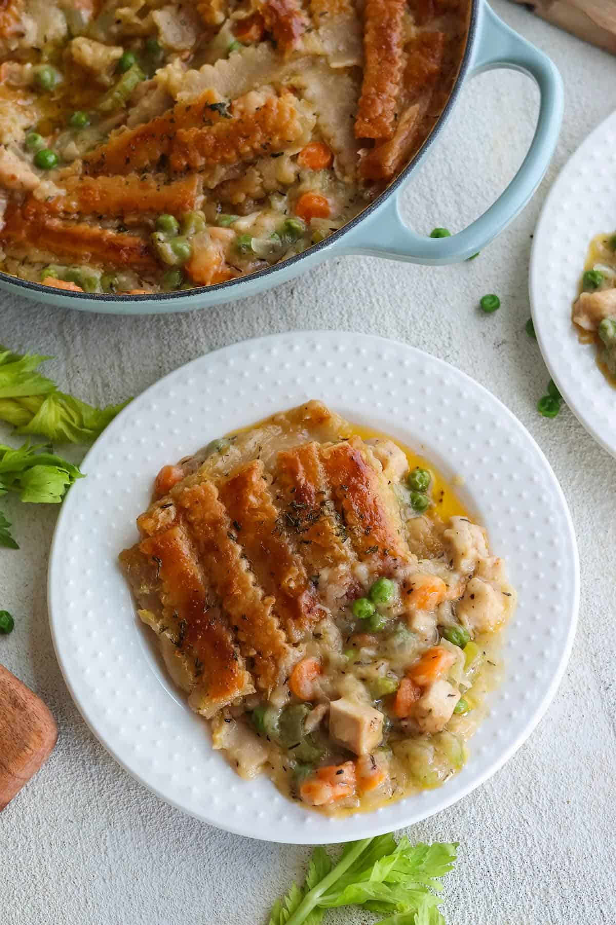A white plate with chicken pot pie next to a skillet with more pot pie.