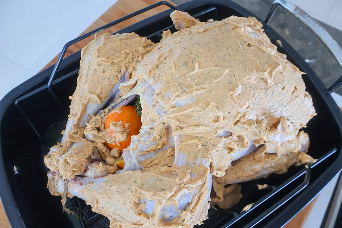 A turkey coated in herbed butter in a black roasting pan. 