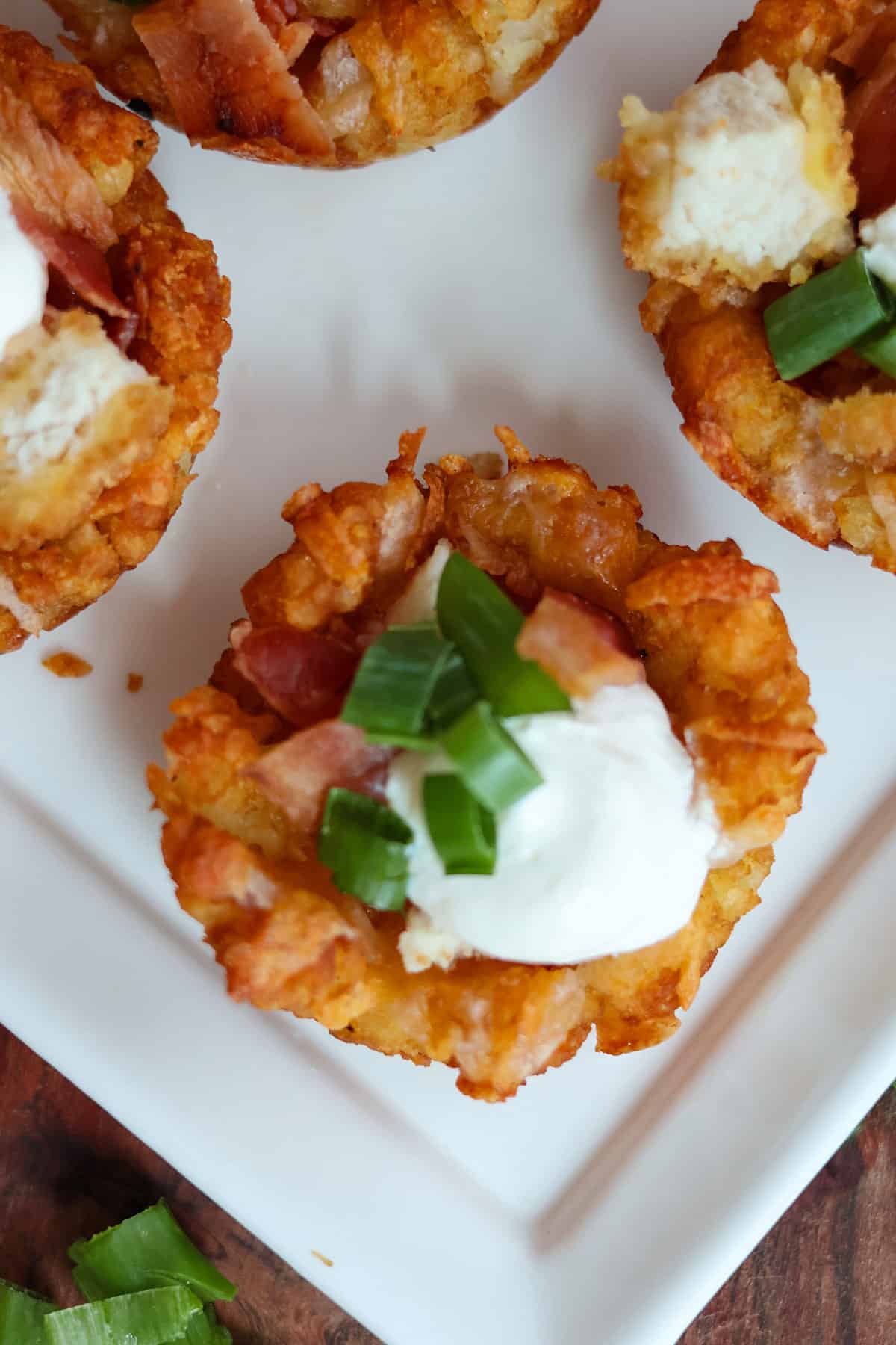 A tater tot cup topped with sour cream on a white plate.