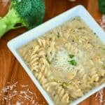 A white bowl of Chicken Alfredo Soup with broccoli in the background.