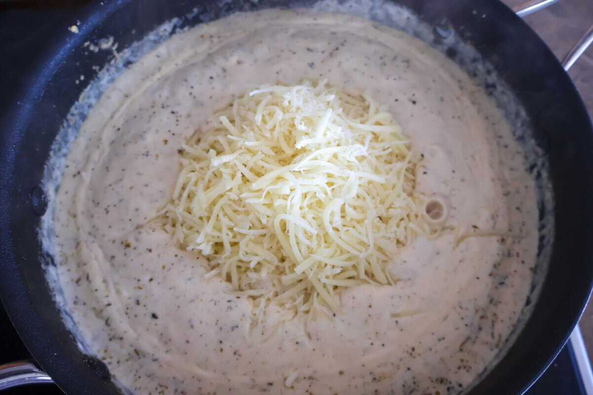 A pile of cheese on top of a cream sauce in a pan.