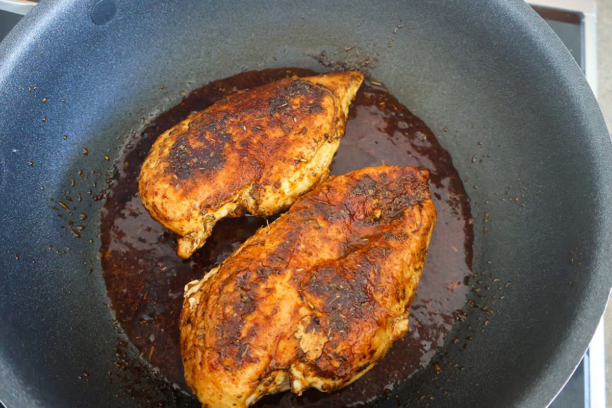 Two seared chicken breasts in a skillet.