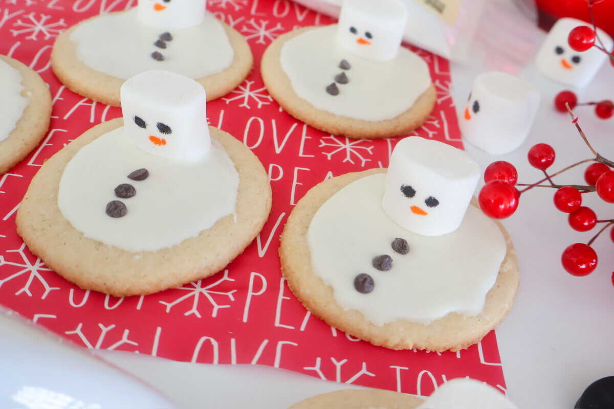 A counter full of Melted Snowman Cookies on red holiday paper.