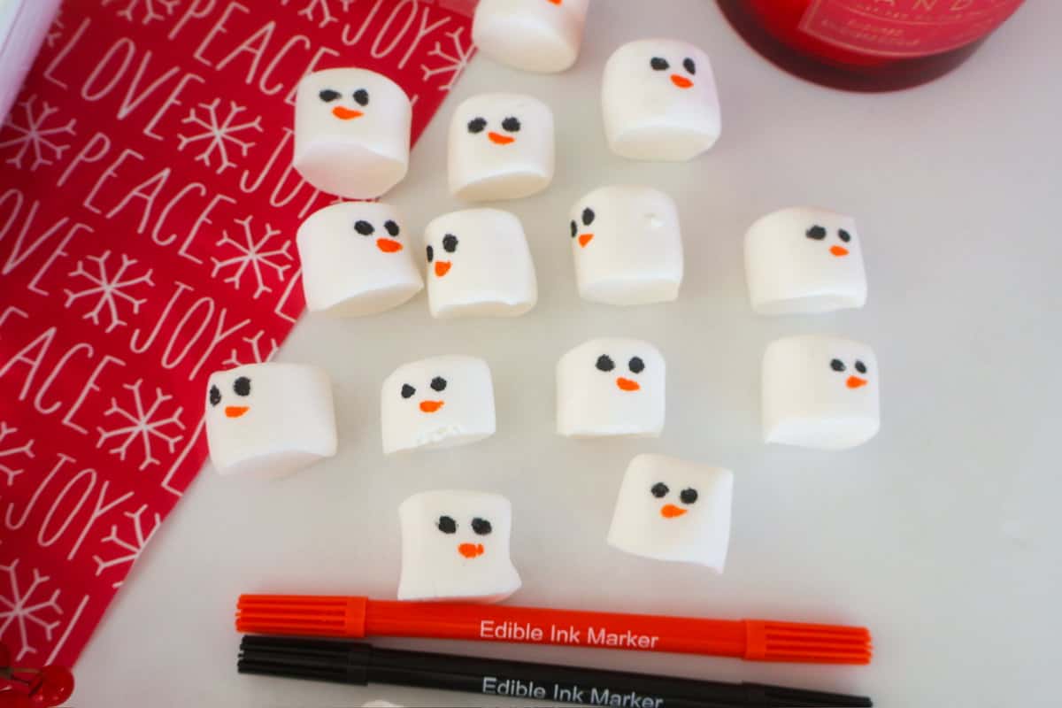 Marshmallows decorated to with food pens to look like snowmen.