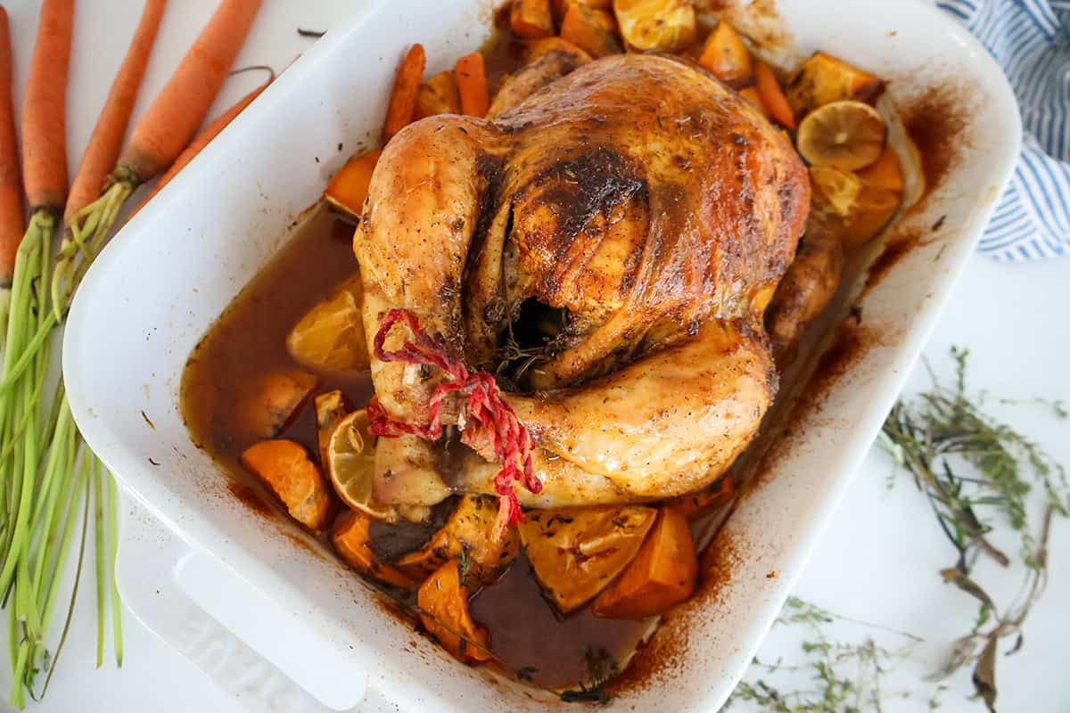 A cooked whole chicken with vegetables in a white baking dish.