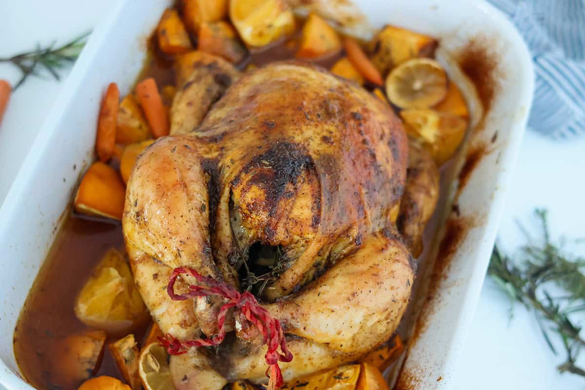 Cooked whole chicken and vegetables in a white baking dish.