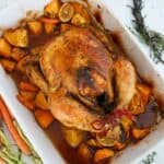 A whole roasted chicken with vegetables in a white baking dish.