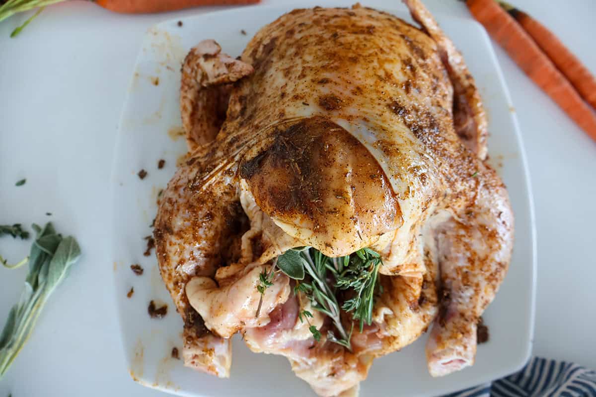 A whole raw chicken seasoned and stuffed with herbs.
