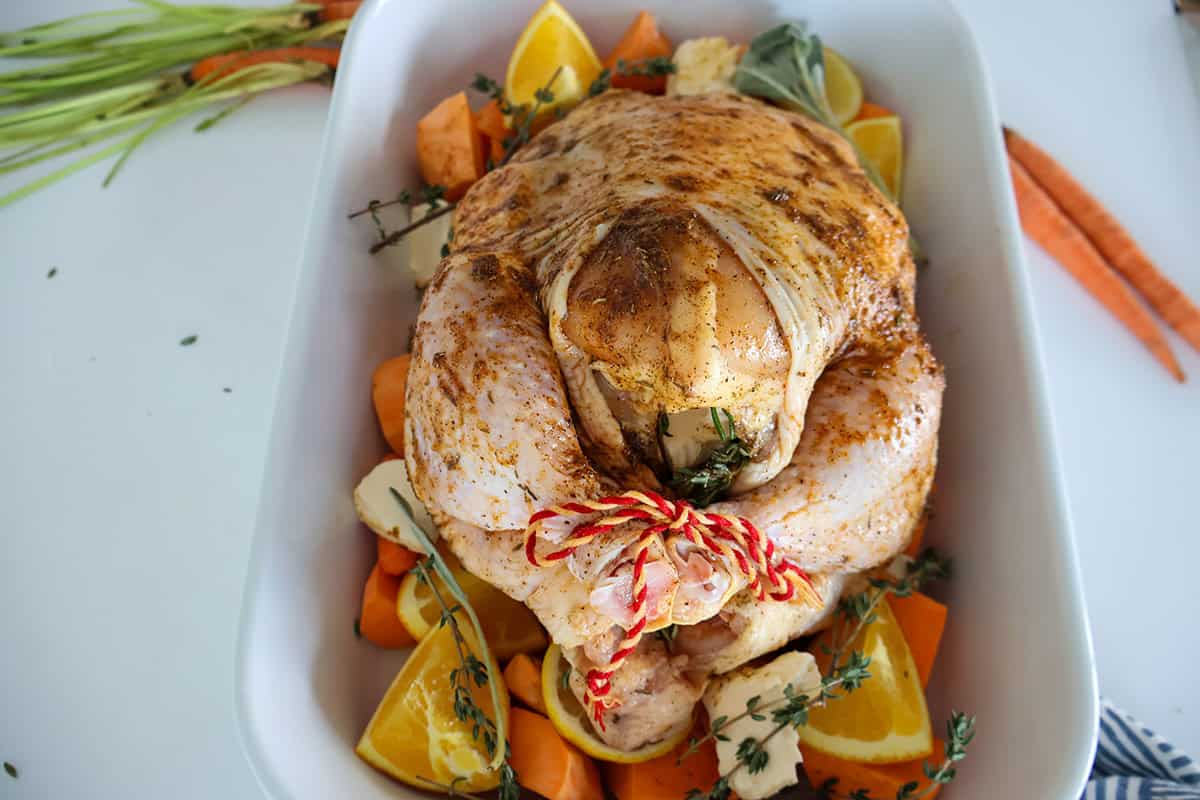 A seasoned whole chicken and vegetables in a white baking dish.