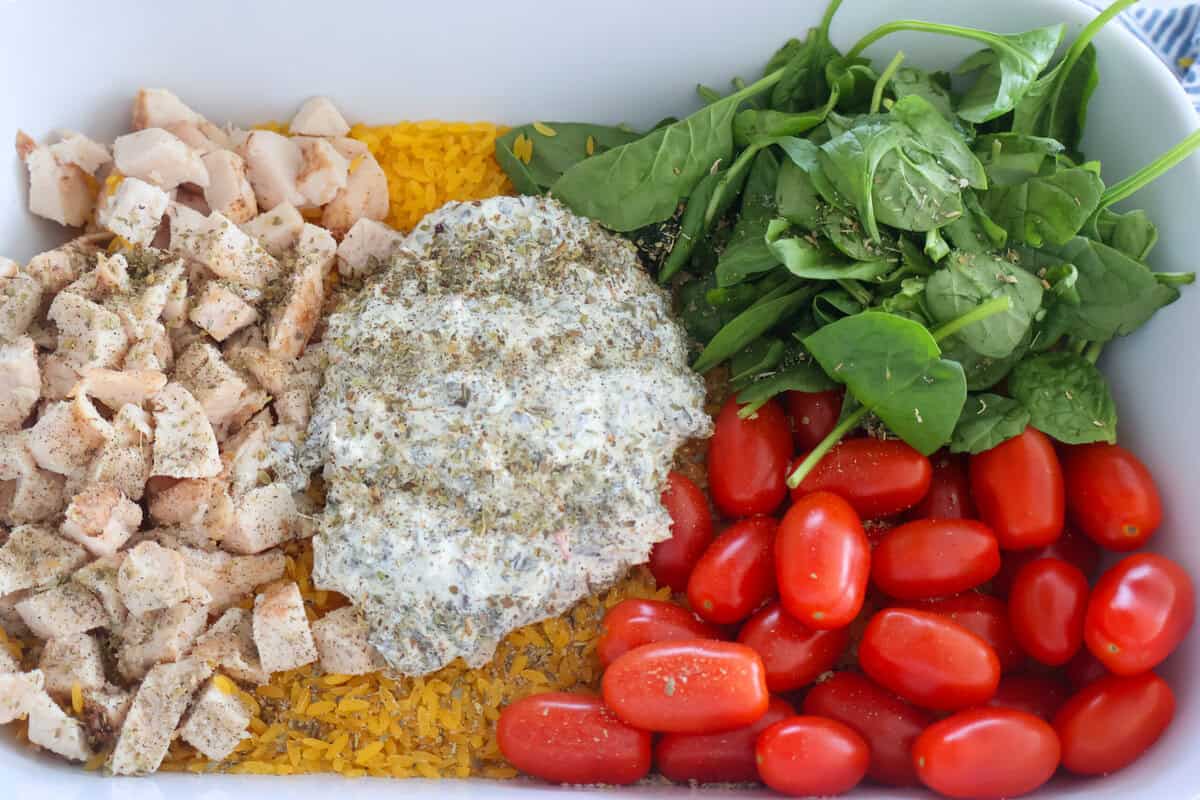 A baking dish with orzo, spinach, chicken, tomatoes and dip in the middle.