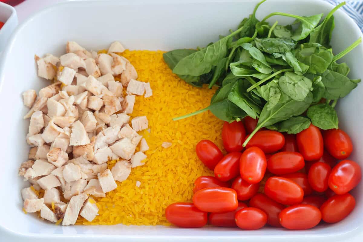 A baking dish of orzo, chicken, tomatoes and spinach.