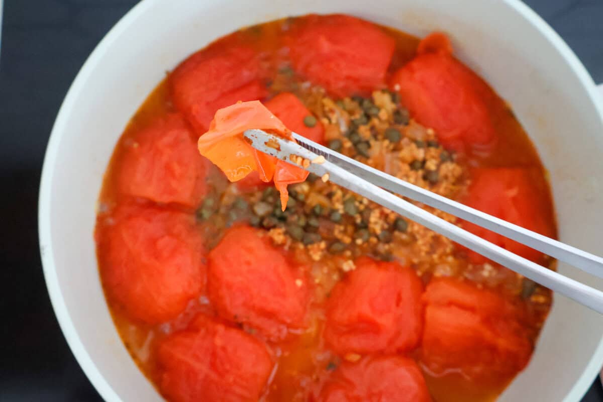 Tongs removing the skin of a tomato for tomato sauce.