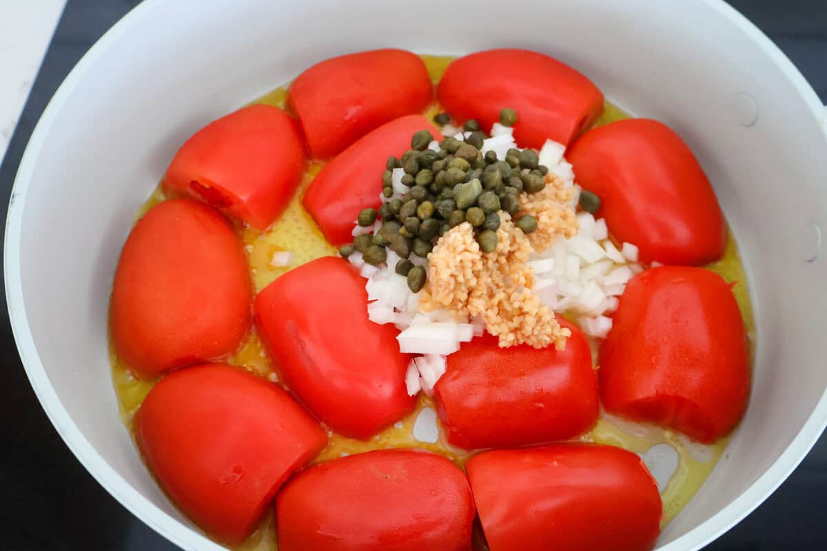 Tomatoes and onions and capers in a saute pan.