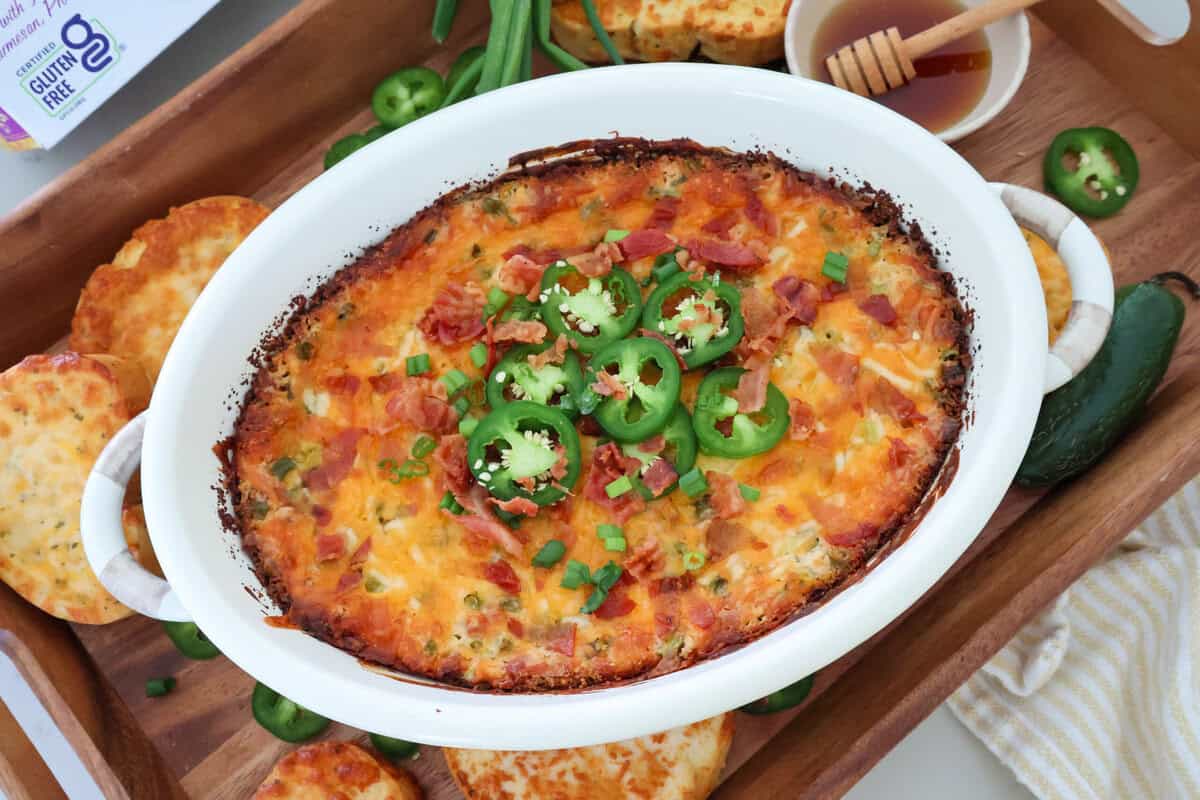 Jalapeño popper dip on a wood tray with toast, peppers, and honey.