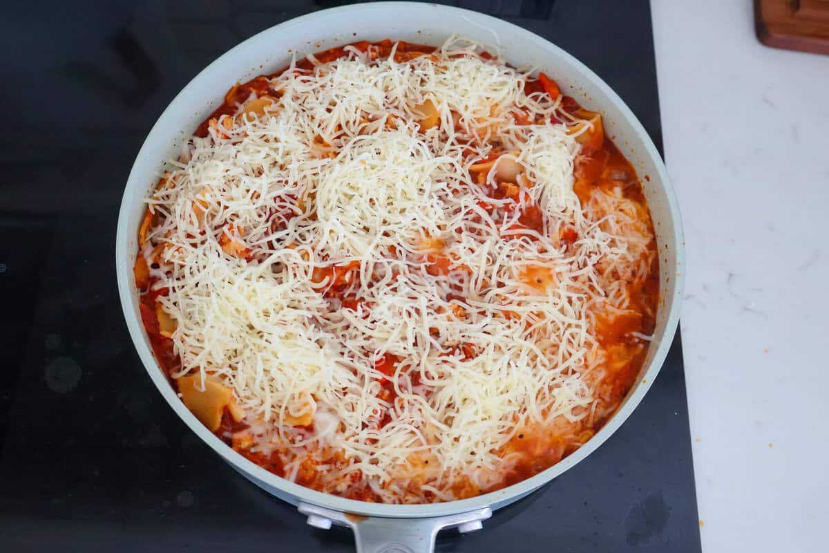 Raw cheese on top of Lazy Lasagna in a saute pan.