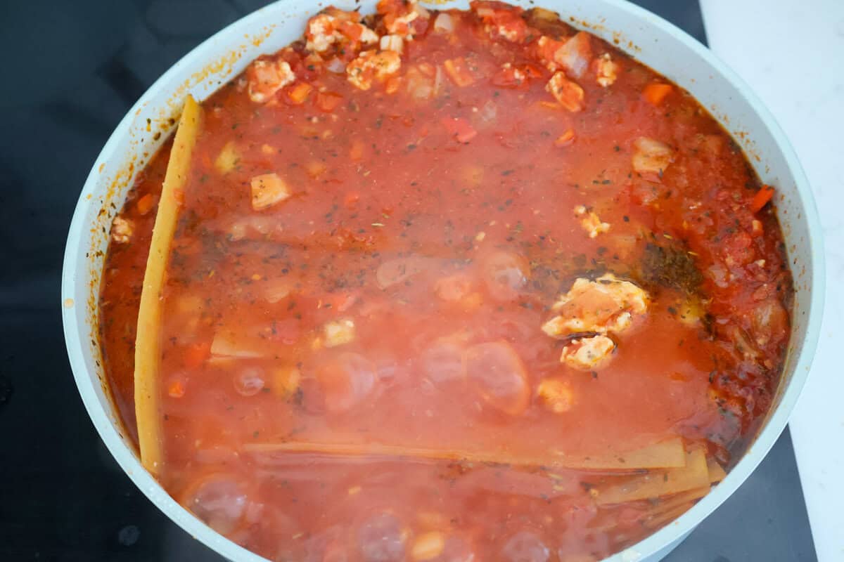 Lasagna noodles in red sauce in a saute pan.