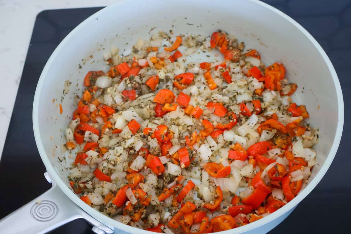 Red bell peppers and onions in a saute pan.