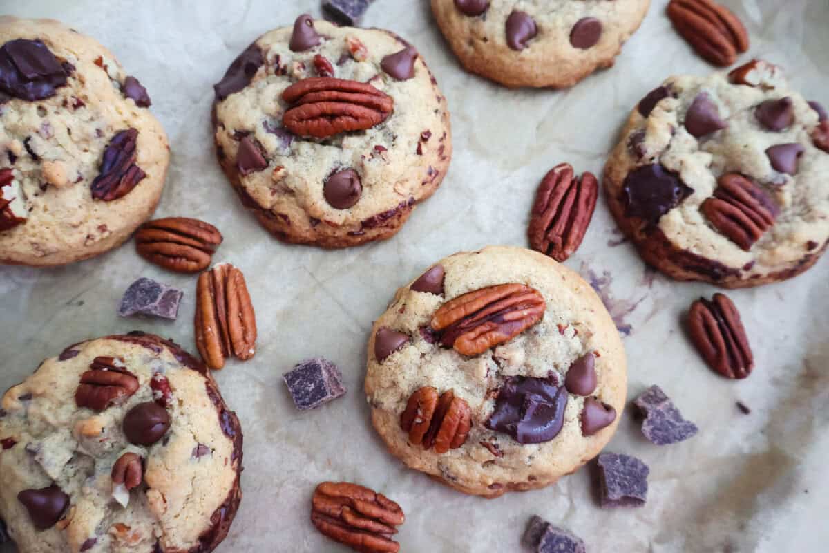 Pecan and Chocolate Chip Cookies on a tray with extra pecans and chocolate chunks.
