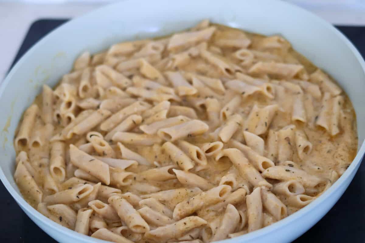 Penne pasta added to a pan of creamy garlic sauce.