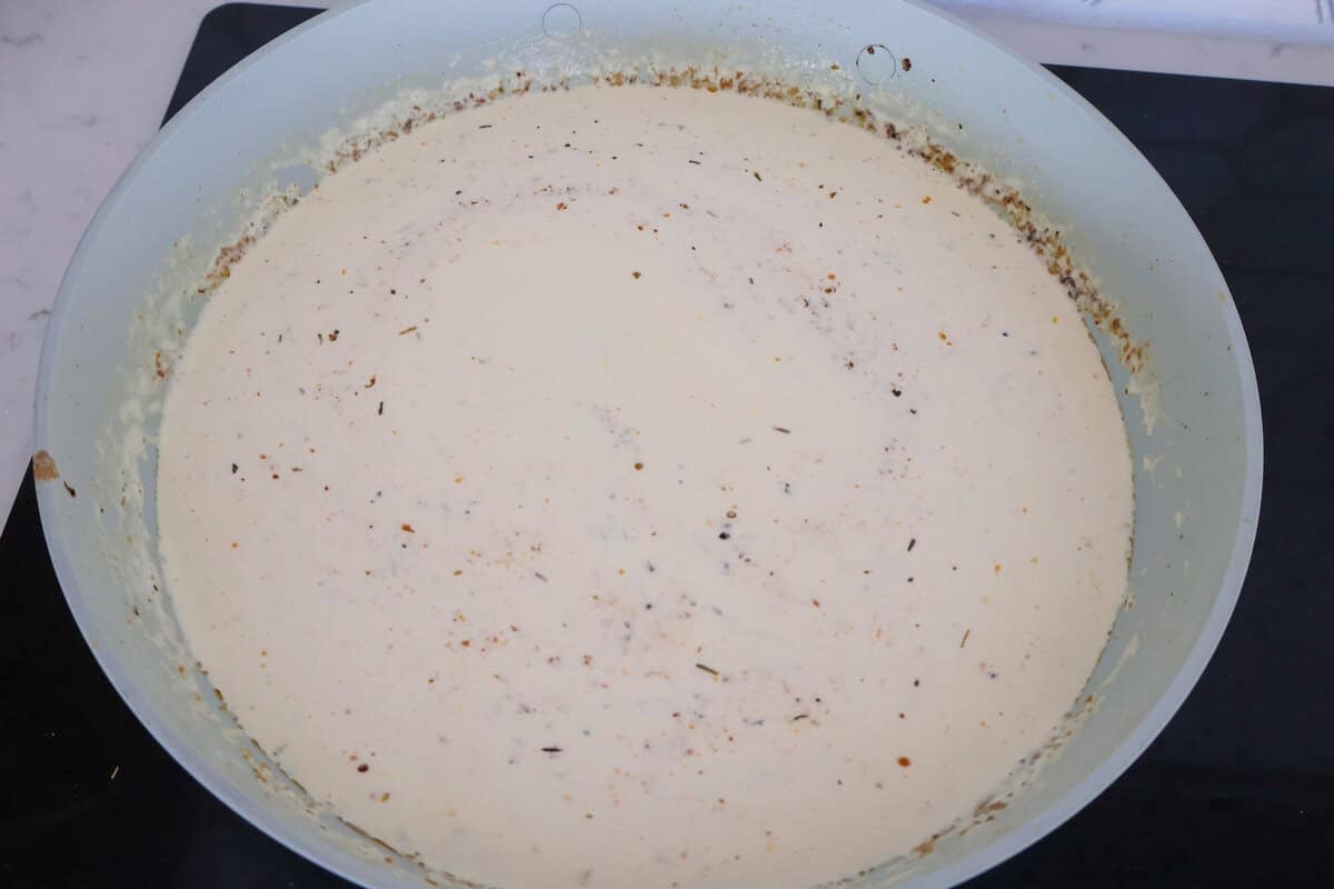 Cooking a white creamy garlic sauce in a skillet.