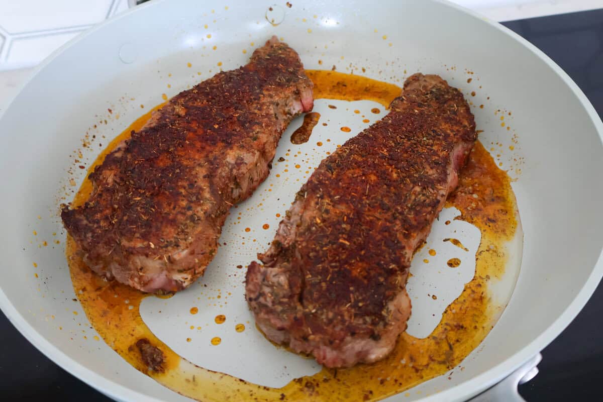 Two cooked New York Strip steaks in a pan.