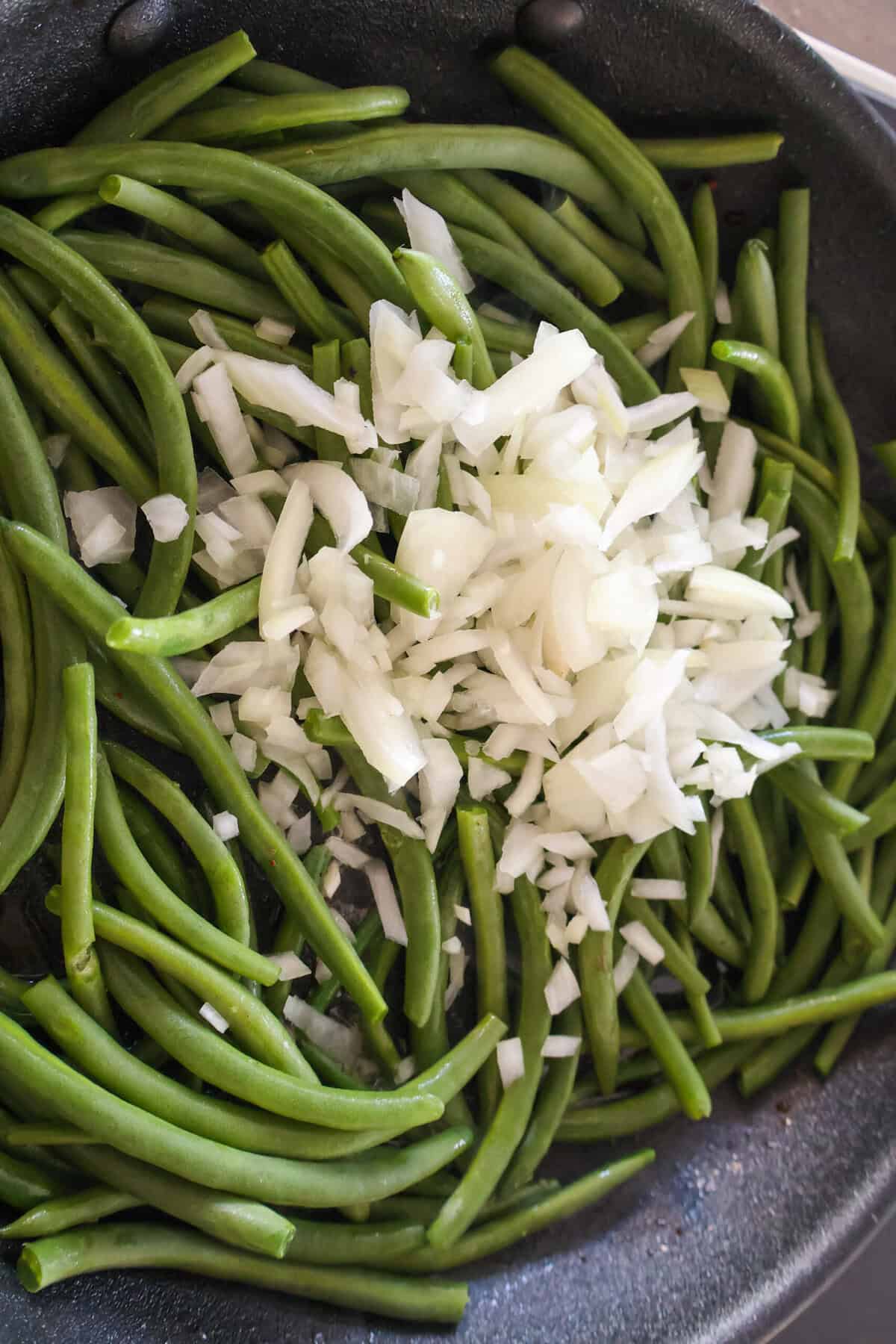 Raw green beans and onion in a saute pan.