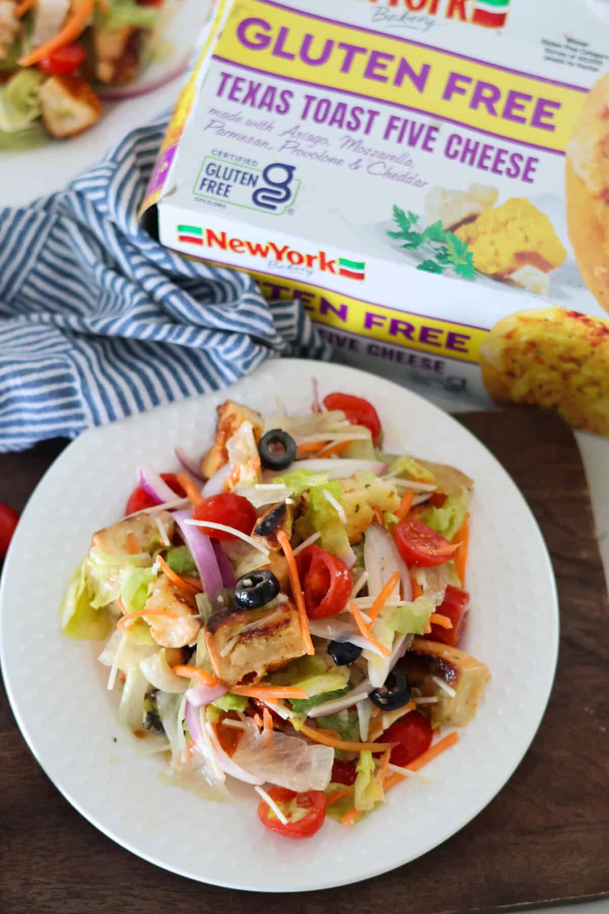 A plate of Copycat Olive Garden Salad with a box of 5 cheese Texas toast in the background.