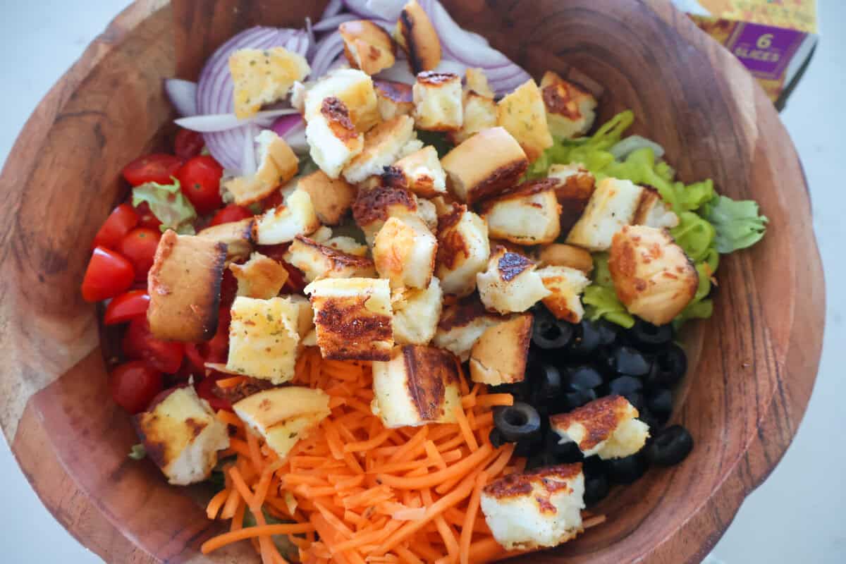 A bowl of salad with croutons, carrots, lettuce, tomatoes, black olives and red onions.