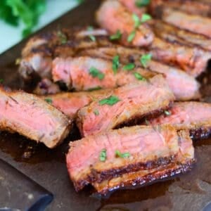 New York Strip steak slices on a brown cutting board with green garnish.