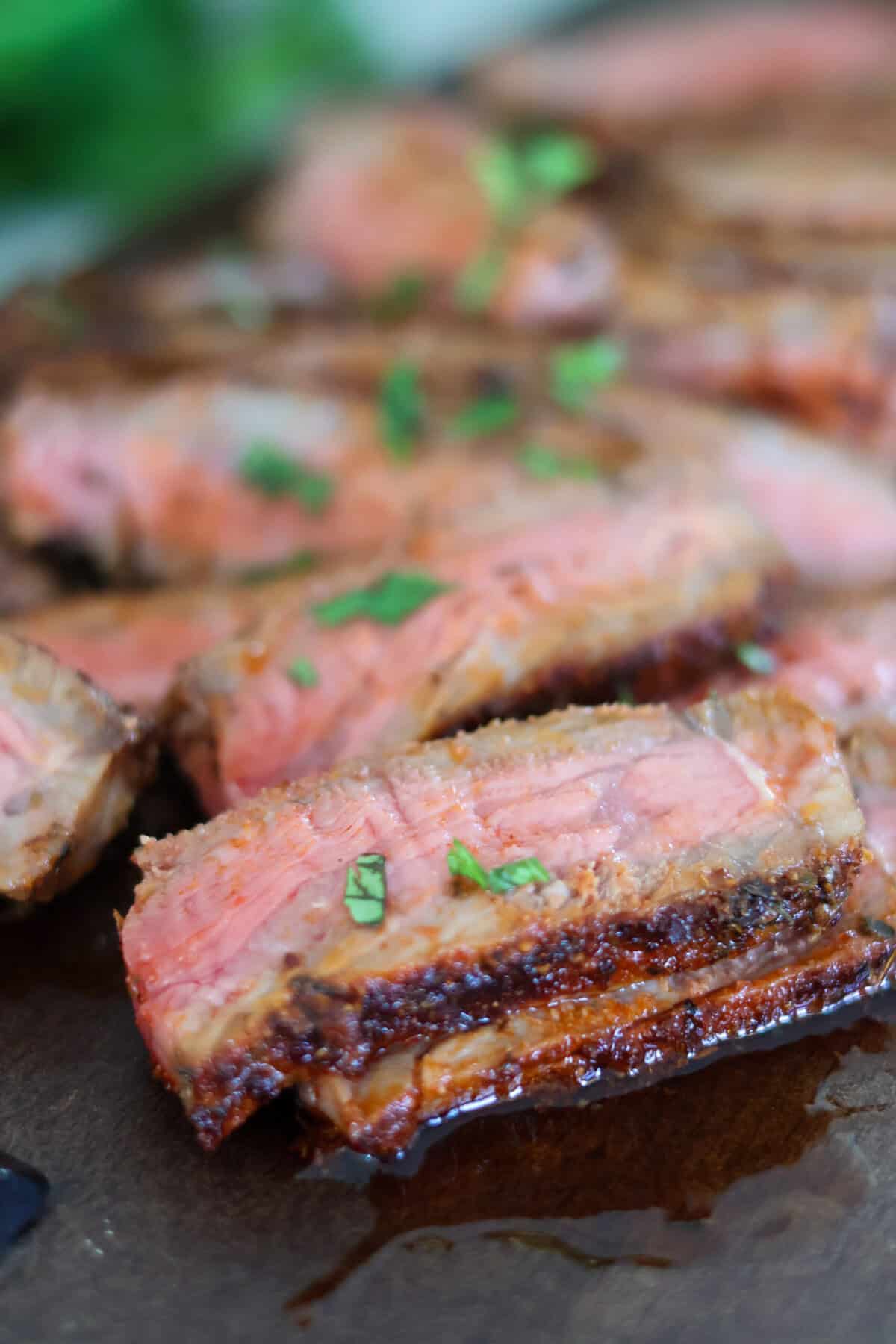 New York Strip steak slices on a brown cutting board with green garnish.