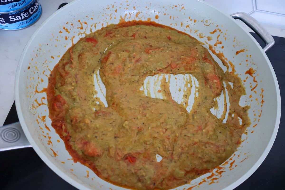 a skillet of cooked tomatoes and pesto sauce cooking together.