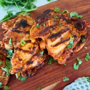 Two George Foreman Chicken Thighs on a wood cutting board with green garnish.