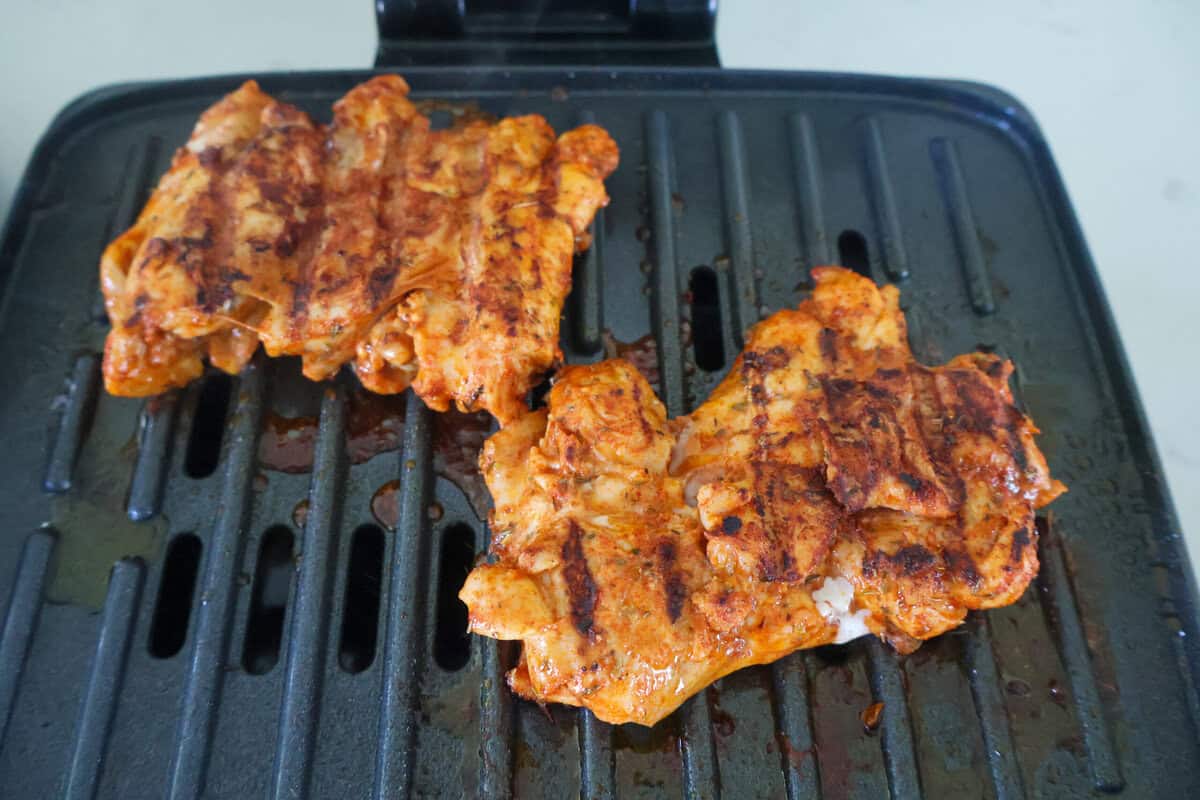 Two chicken thighs with grill marks cooking on a George Foreman grill.