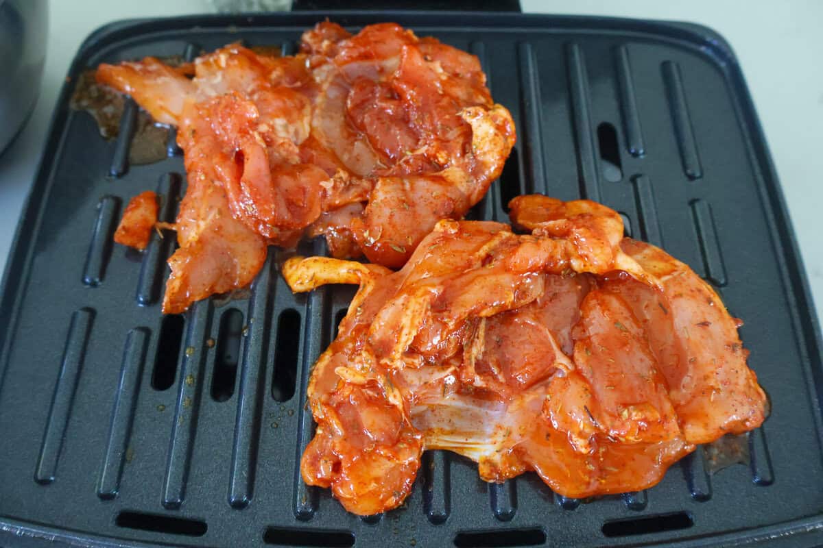Two marinated chicken thighs cooking on a George Foreman Grill.