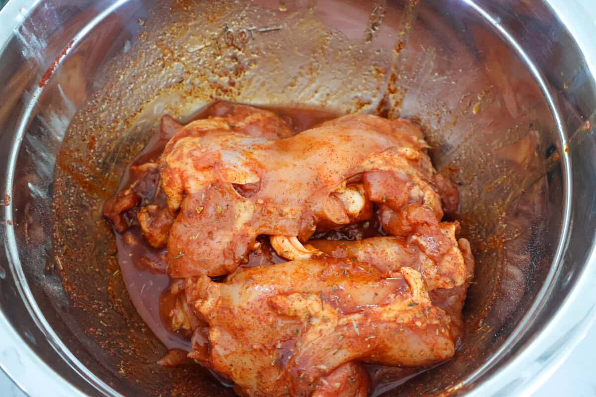 raw chicken thighs marinating in a metal bowl.